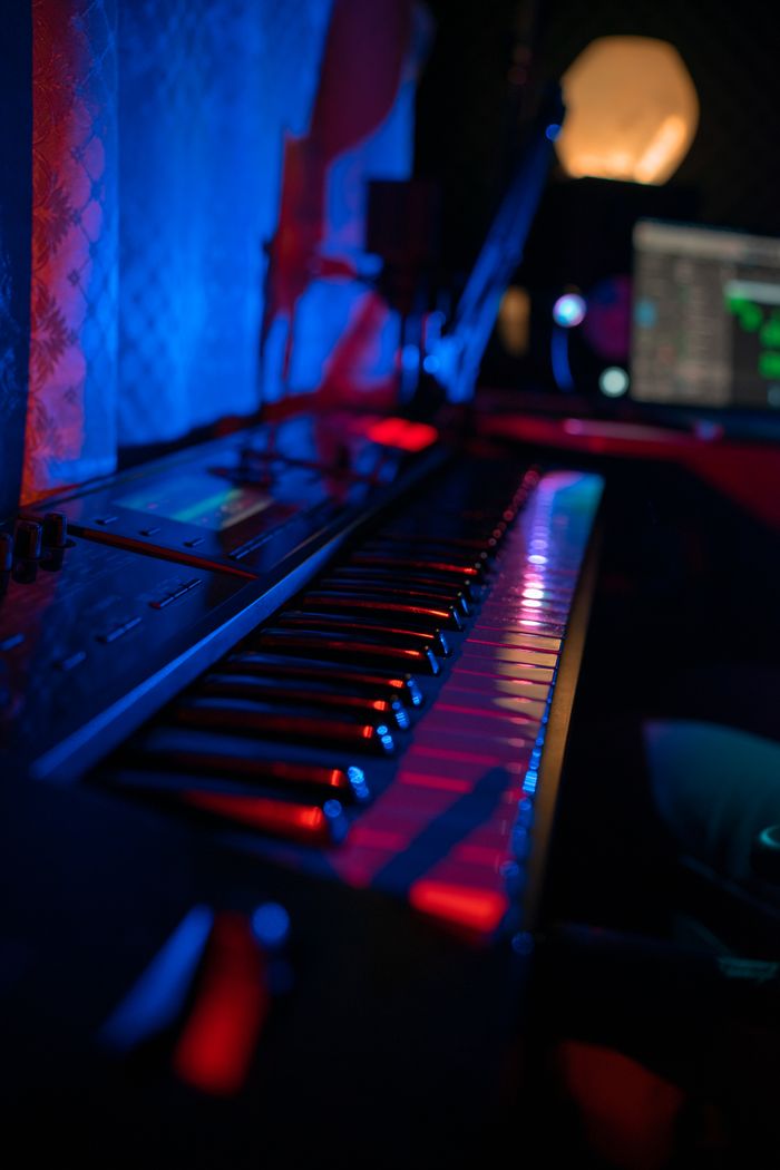 Moody music studio featuring a synthesizer keyboard and computer screen with neon lighting.